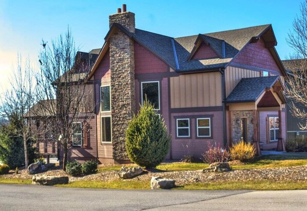 A two-story house with a stone chimney, large windows, and a well-maintained lawn.