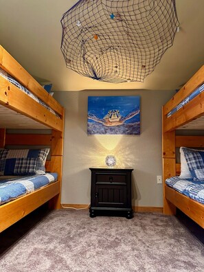 Une chambre avec deux lits superposés, une petite commode noire, un tableau représentant une tortue de mer et un luminaire au plafond.