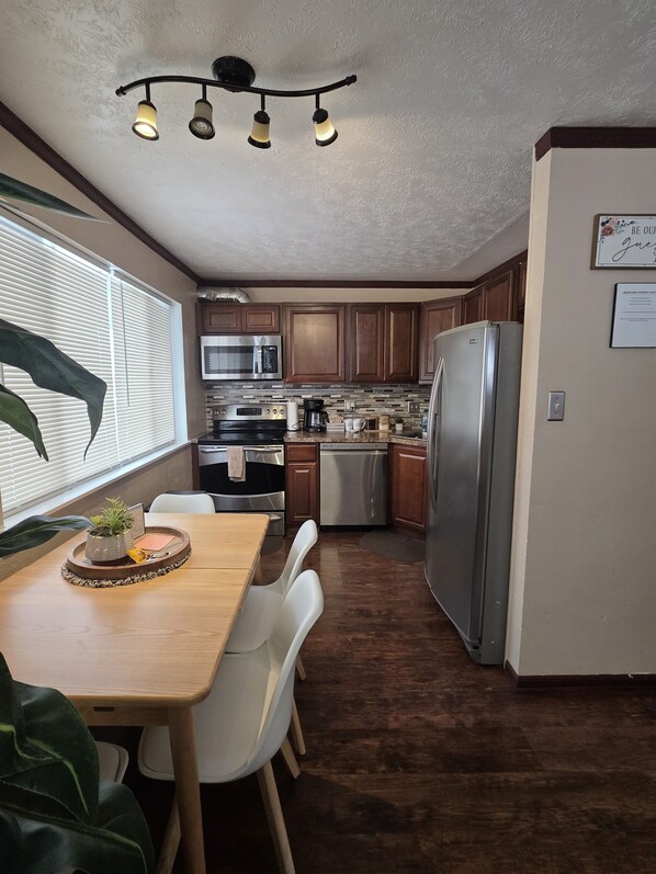 A compact kitchen with a dining area, wooden cabinets, stainless steel appliances, and a ceiling light fixture. - Last frontier Rental Family #3 (Anchorage)