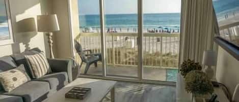 A room with a large sliding glass door leading to a balcony with a view of the beach.