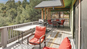 Une terrasse en bois avec des meubles d’extérieur, un espace salon couvert et une vue sur une zone boisée.