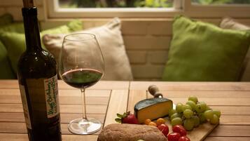 A wooden table with a wine bottle, a glass of red wine, a loaf of bread, a cheese, and a variety of grapes and tomatoes.