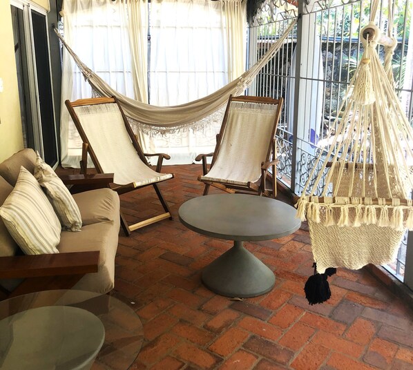 Un espacio al aire libre acogedor con una hamaca, dos sillones con cojines, una mesa redonda y una lámpara colgante.