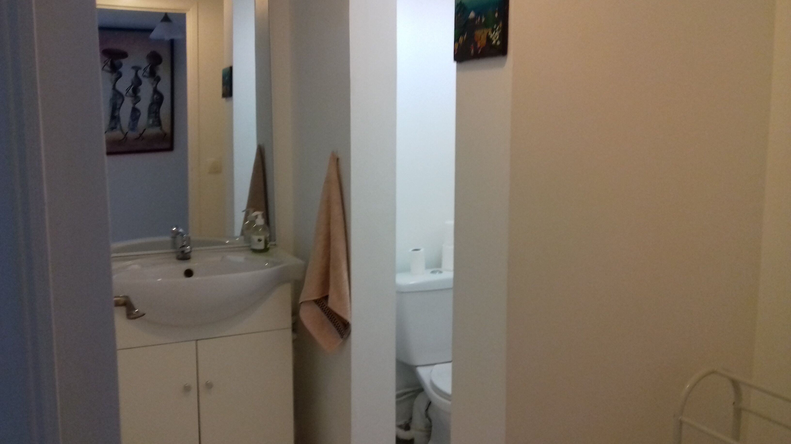 A bathroom with a sink, mirror, towel rack, toilet, and a painting on the wall.