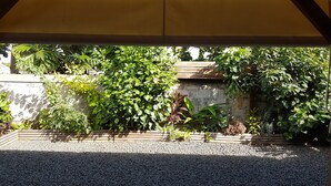 Un espace extérieur abrité, doté d’un sol en gravier, entouré de différentes plantes et d’un mur en pierre.