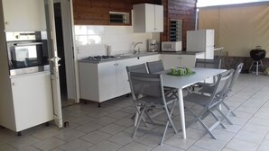 Une cuisine compacte avec des meubles blancs, une cuisinière à gaz, un four à micro-ondes et un réfrigérateur. On y trouve une table à manger avec des chaises et un plateau vert avec des tasses.