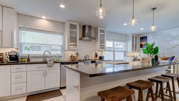 A modern kitchen with white cabinetry, a large island with stools, and pendant lighting. - Safety Harbor Paradise (Safety Harbor)