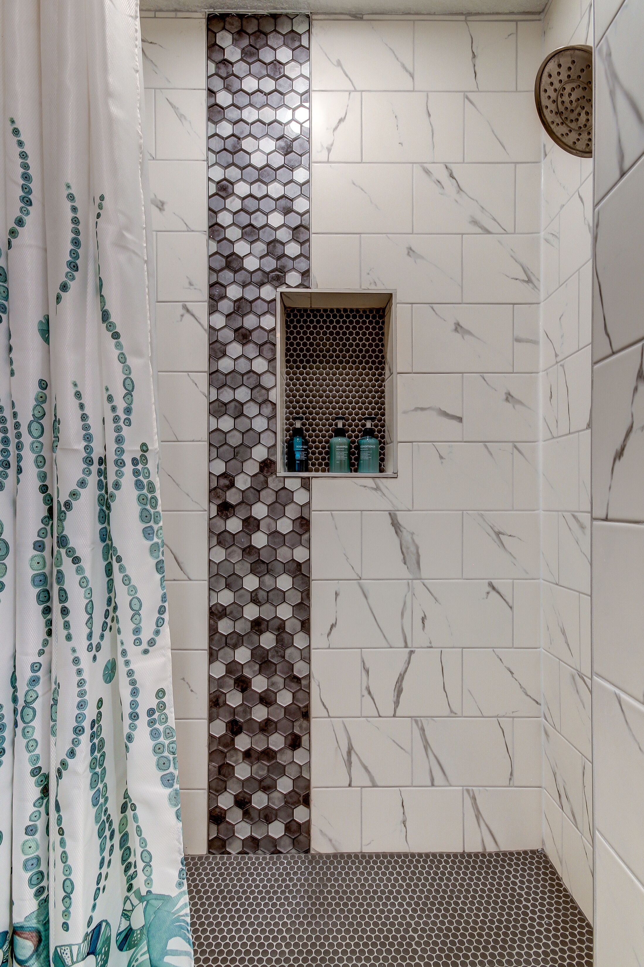A shower area with a tiled wall featuring a honeycomb pattern and a shelf with toiletries.