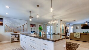 A modern kitchen with white cabinetry, a central island, pendant lighting, and a large window. - Safety Harbor Paradise (Safety Harbor)