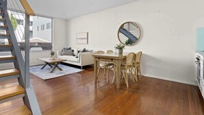 A modern living room with a wooden staircase, a dining area with wicker chairs, and a large mirror on the wall.