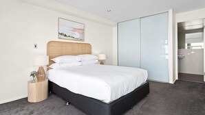 A modern hotel room with a large bed, a bedside table with a lamp, a wall-mounted painting, and a sliding door leading to a bathroom.