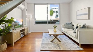A modern living room with a wooden staircase, a large window with a view, a white sofa, and a coffee table.