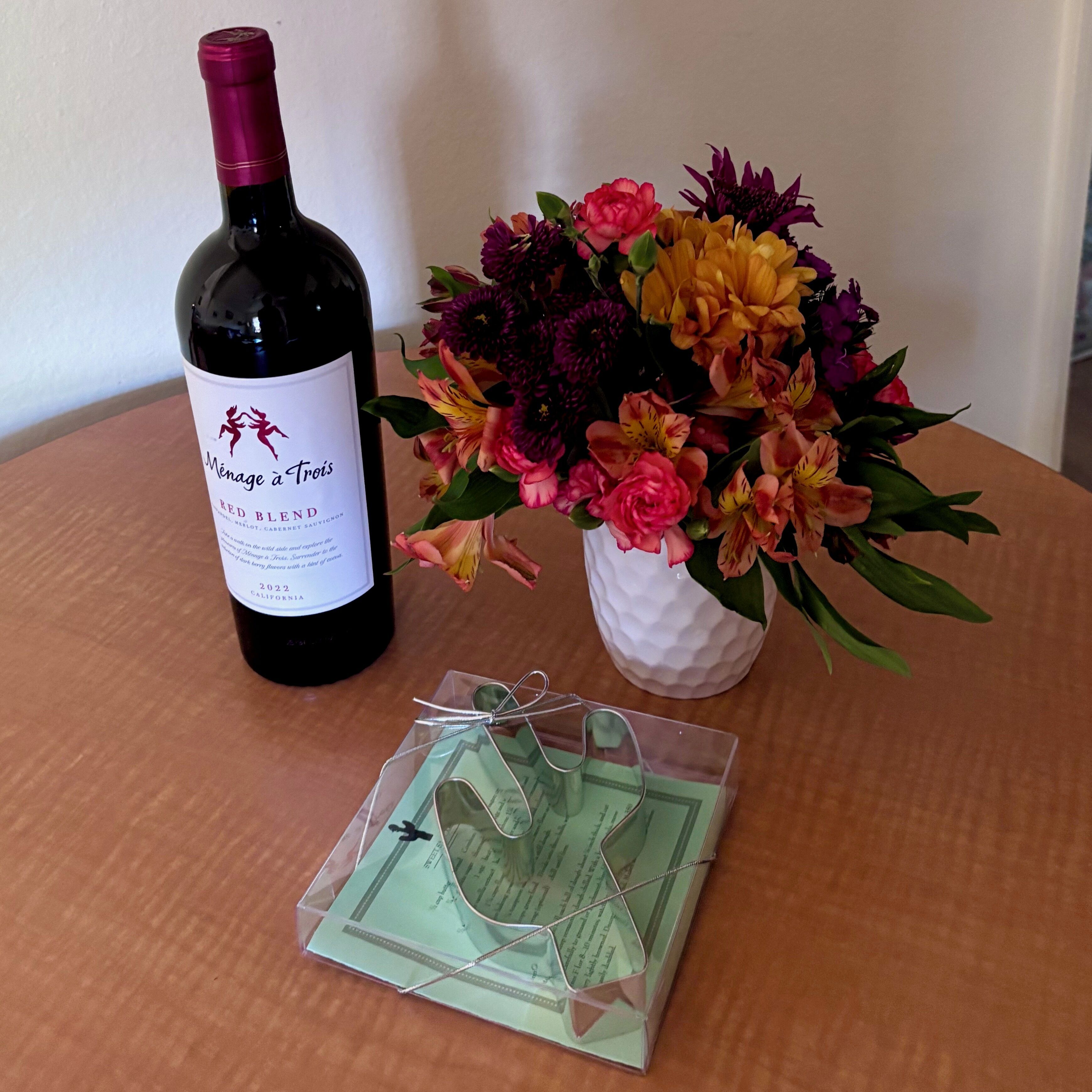A bottle of wine, a bouquet of flowers, and a pair of glasses on a table.