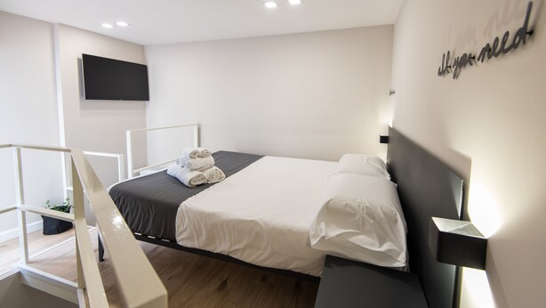 A modern hotel room with a bed, a flat-screen TV mounted on the wall, and a bedside table with a lamp. - Five Boutique Rooms - Camera 1 (Naples)