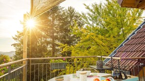 A round table with wicker chairs on a wooden deck, overlooking a forested area with a view of the ocean. - Graine de Bonheur gite ambiance chalet 7 persons (Chille)