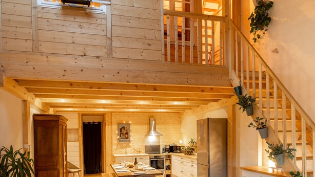 A spacious loft-style living area with a high ceiling, wooden beams, a staircase, a kitchen, and a cozy seating area with a sofa and coffee table. - Graine de Bonheur gite ambiance chalet 7 persons (Chille)