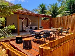 Una terraza de madera con muebles de exterior, que incluye una mesa y sillas, y una hamaca colgante.