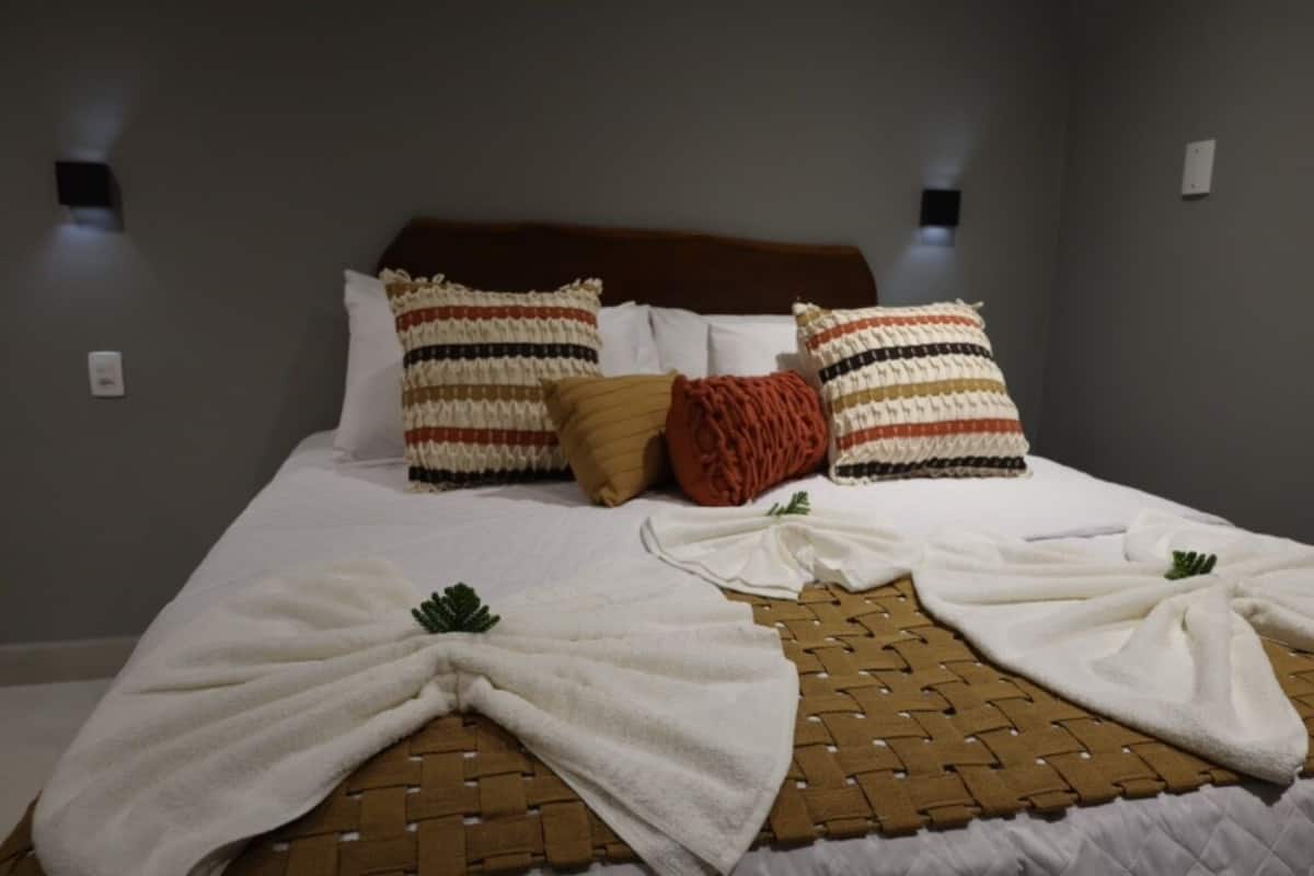 Uma cama bem arrumada com um cobre-leito marrom trançado, travesseiros brancos e um cobertor vermelho.