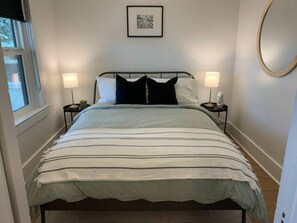 A neatly made bed with a striped bedspread, two bedside lamps, and a framed picture on the wall. - Six Two Nine (Brandon)
