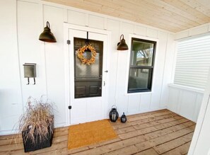 A wooden porch with a white door, a wreath, and two lanterns. - Six Two Nine (Brandon)