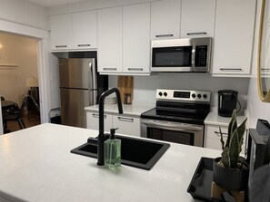 A modern kitchen with white cabinets, stainless steel appliances, and a black countertop. - Six Two Nine (Brandon)