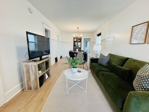 A modern living room with a green sofa, a white coffee table, and a flat-screen TV on a wooden stand. - Six Two Nine (Brandon)