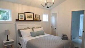 Une chambre à coucher comprenant un lit, une table de chevet, une lampe et une porte donnant sur une autre pièce.