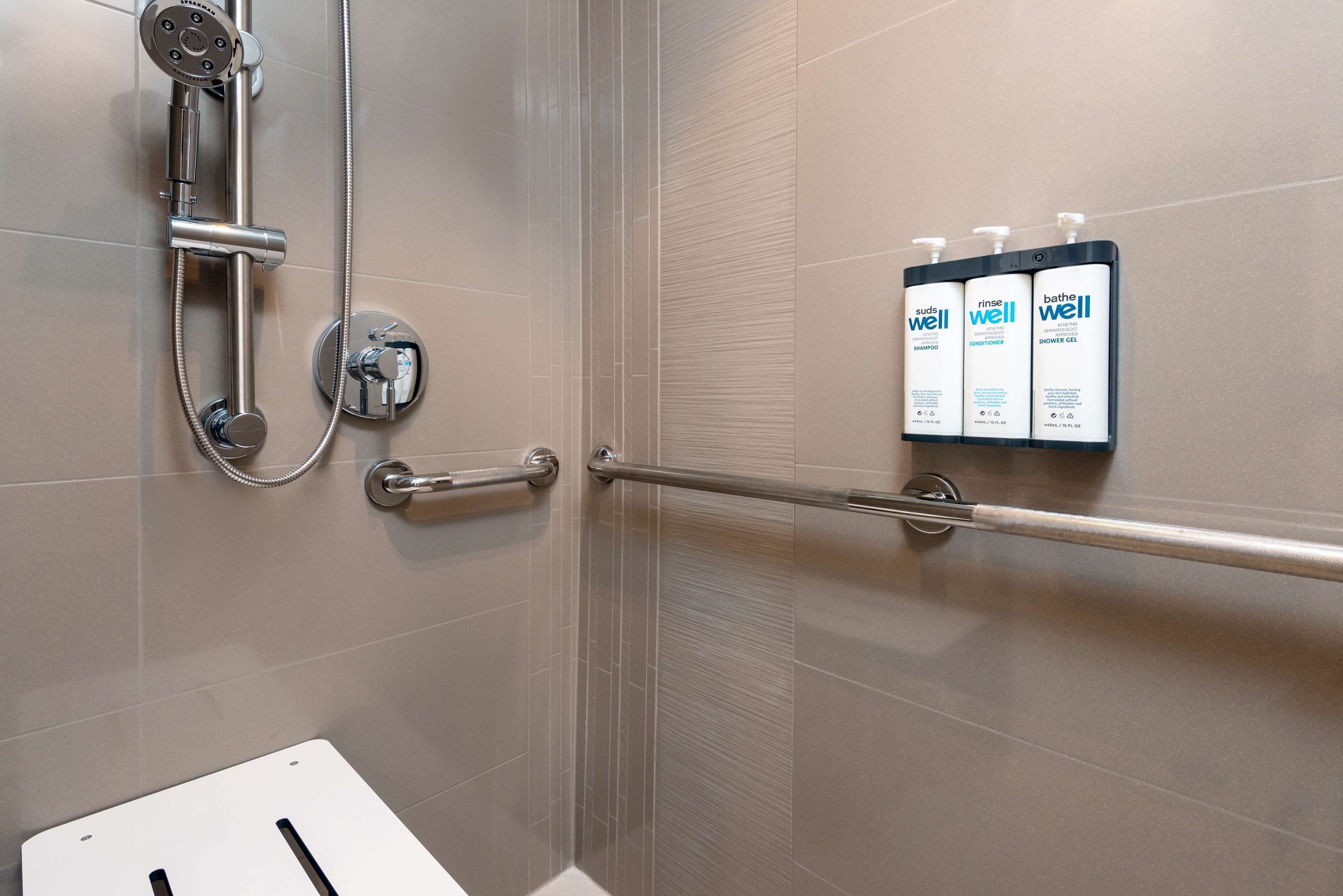 A shower area with a handheld showerhead, a towel rack, and a set of toiletries including shampoo, conditioner, and body wash.