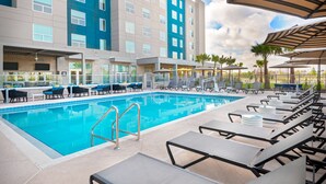 A swimming pool with lounge chairs and umbrellas, surrounded by a multi-story building with balconies. - Hyatt House Orlando Airport (Orlando)