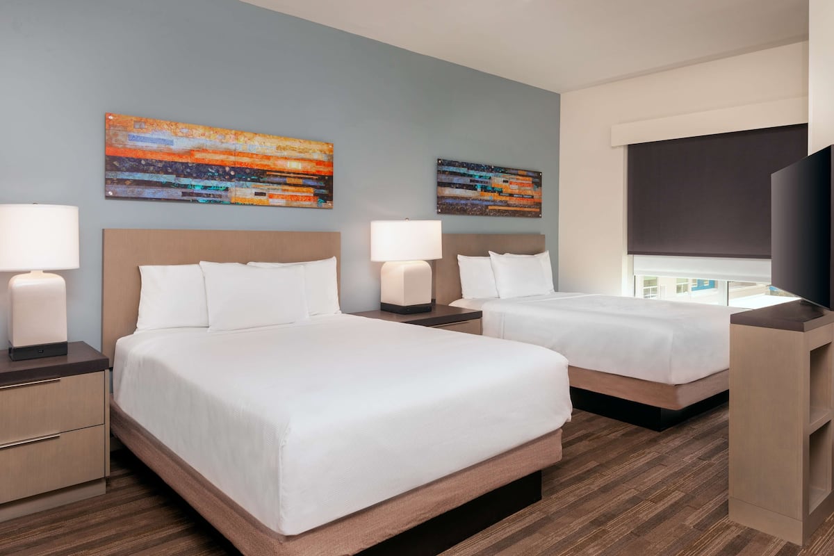 A hotel room with two beds, nightstands, lamps, and artwork on the walls.