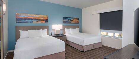 A hotel room with two beds, a desk, a TV, and artwork on the walls.