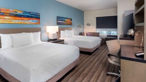 A hotel room with two beds, a desk, a chair, a lamp, and two paintings on the wall. - Hyatt House Orlando Airport (Orlando)
