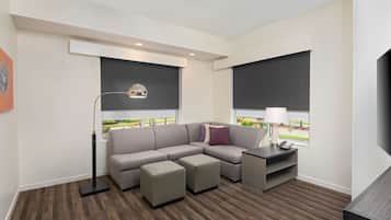 Un salon moderne avec un canapé d’angle, des poufs, une lampe sur pied, une table d’appoint avec une lampe et un téléviseur.