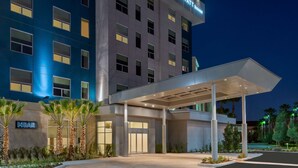 A modern hotel with a blue facade, a covered entrance, and palm trees in the foreground. - Hyatt House Orlando Airport (Orlando)