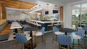 A modern bar area with a long counter, bar stools, and a seating area with tables and chairs. - Hyatt House Orlando Airport (Orlando)