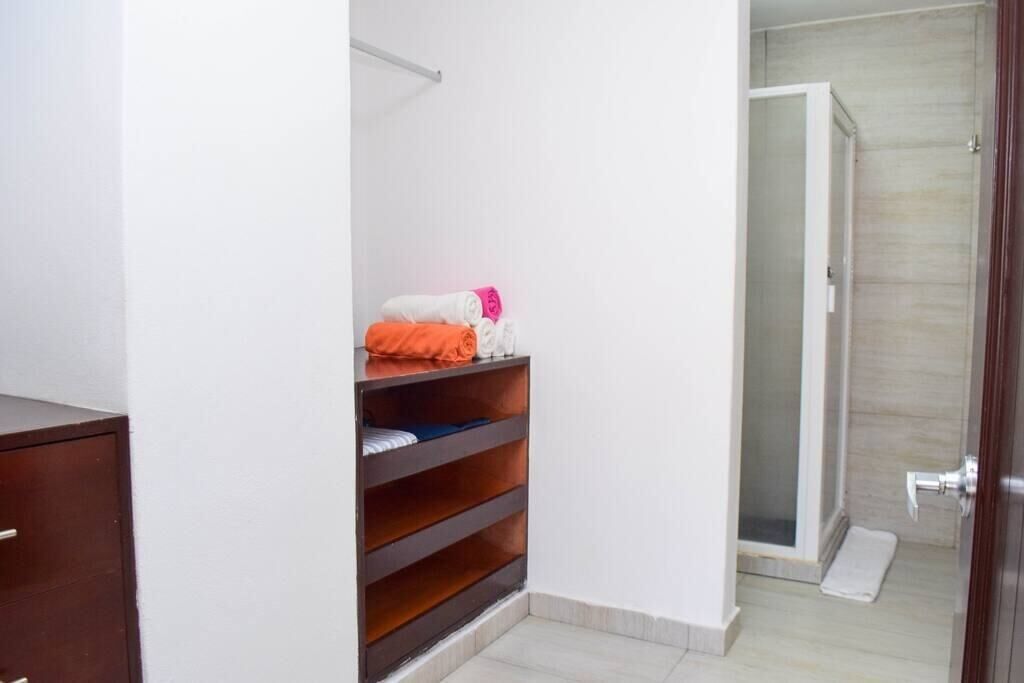 A bathroom with a shower, a towel rack, and a wooden shelf with folded towels.