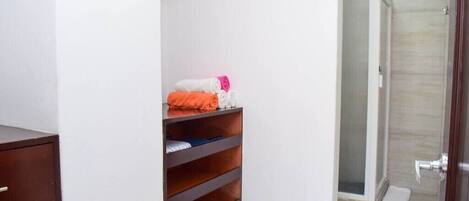A bathroom with a shower, a towel rack, and a wooden shelf with folded towels.