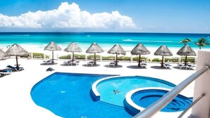 A pool area with a view of the ocean, lounge chairs, and thatched umbrellas. - Beautiful 2 levels apartment at the best beach area of Cancun hotel zone.... (Cancún)