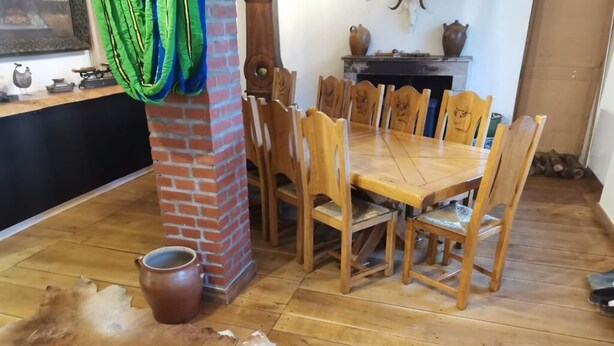 Un área de comedor con una mesa y sillas de madera, un pilar de ladrillo y un cuero en el suelo.