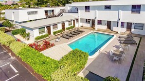 Un hotel moderno con piscina en la azotea, tumbonas y un jardín bien cuidado.