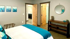 Een slaapkamer met een bed, een houten bankje, een ronde spiegel en drie aan de muur hangende schilderijen.