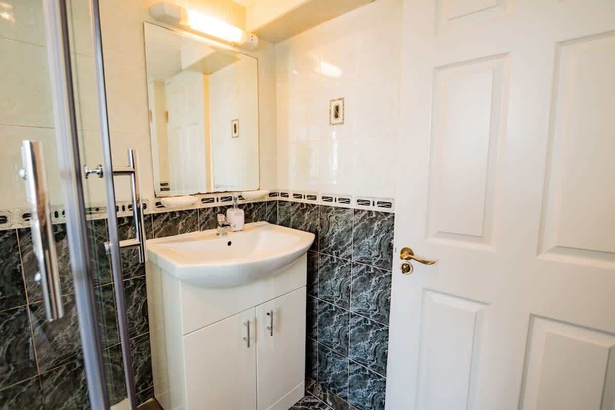 Une salle de bain avec un lavabo blanc, une douche en verre et un pare-baignoire en marbre.