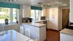 Una cocina moderna con armarios blancos, una isla central y un comedor con mesa de vidrio.