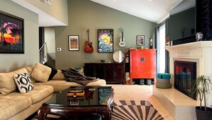 Una sala de estar con sofá, mesa de centro y chimenea. Hay cuadros enmarcados en la pared y una guitarra colgada.