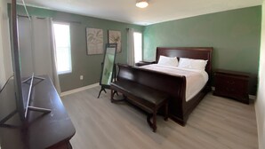 Une chambre à coucher avec un lit, un banc, un meuble pour la télévision et des œuvres d’art accrochées aux murs.