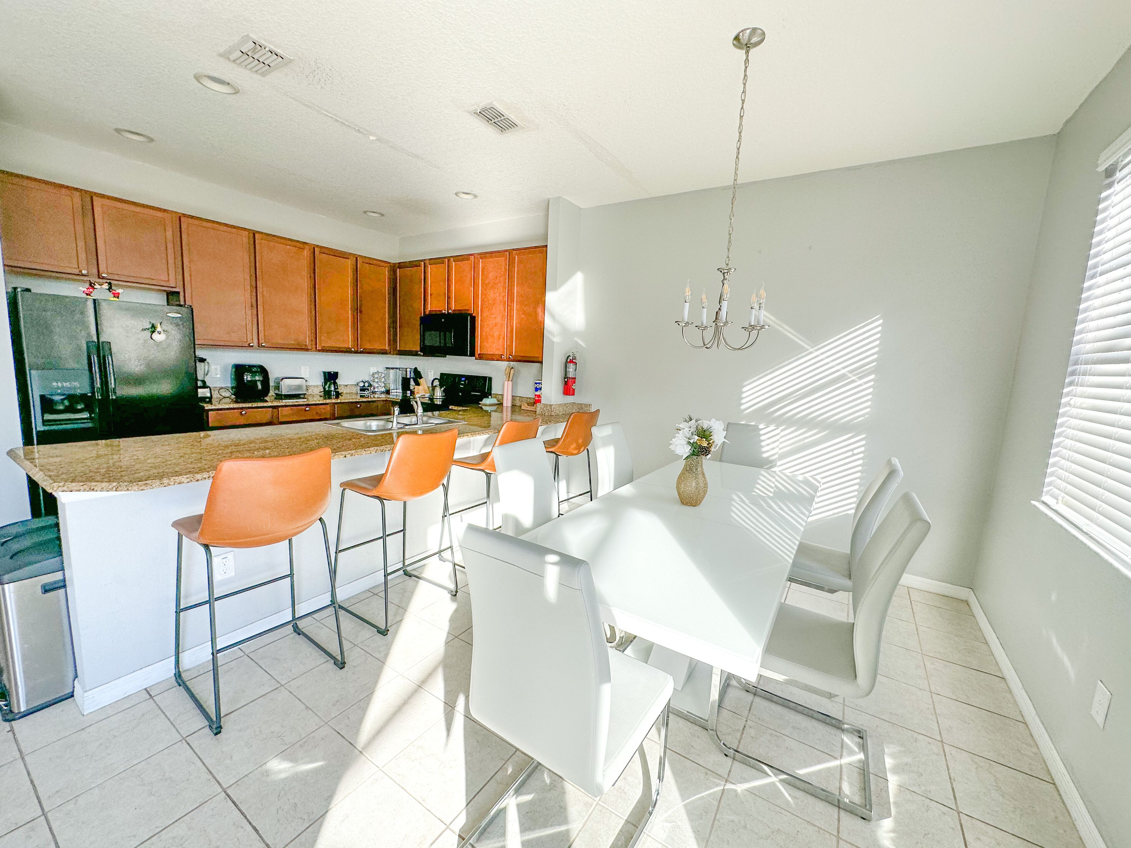 A modern kitchen with a central island, white dining table, and orange chairs.
