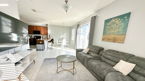 Un salon moderne avec un canapé gris, une table basse et un coin repas avec des chaises blanches.