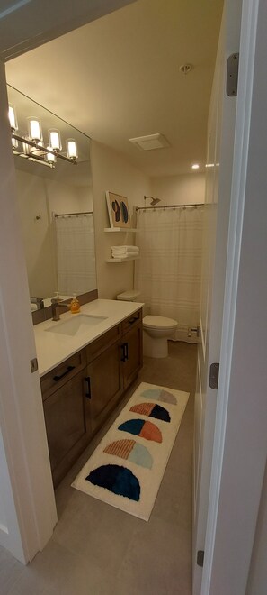 Une salle de bain équipée d’un lavabo, d’un miroir, d’un porte-serviettes, de toilettes, d’un rideau de douche et d’un tapis aux couleurs vives.