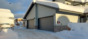 Un bâtiment doté d’une porte de garage, entouré d’un sol recouvert de neige et surplombé d’un ciel dégagé.