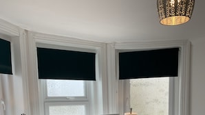 A bedroom with a bed, two bedside tables, a window with blinds, a hanging light fixture, and a plant. - Stunning 3-bed Apartment in Ventnor (Ventnor)